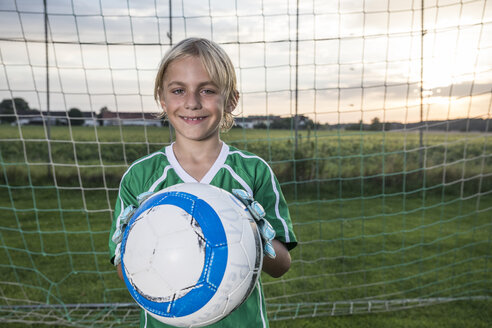 Porträt eines lächelnden jungen Fußballtorwarts, der einen Ball auf einem Fußballplatz hält - WESTF24056