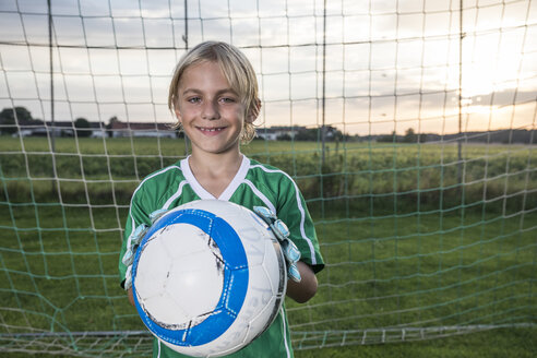Portrait of smiling young football goalkeeper holding ball on football ground - WESTF24056