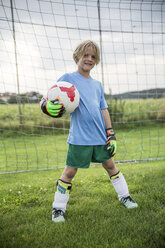 Portrait of smiling young football goalkeeper holding ball on football ground - WESTF24057