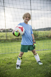 Porträt eines lächelnden jungen Fußballtorwarts, der einen Ball auf einem Fußballplatz hält - WESTF24057