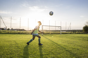 Junger Fußballspieler köpft den Ball auf dem Fußballplatz bei Sonnenuntergang - WESTF24059