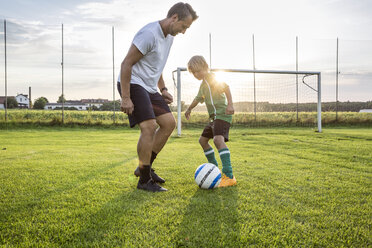 Coach and young football player on football ground at sunset - WESTF24061