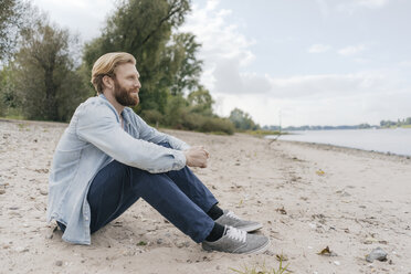 Germany, Duesseldorf, relaxed man sitting on the beach looking at view - KNSF03657