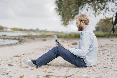 Deutschland, Düsseldorf, Mann sitzt am Strand und benutzt Laptop - KNSF03658
