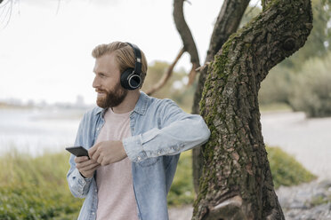 Germany, Duesseldorf, man with smartphone and headphones listening music outdoors - KNSF03659