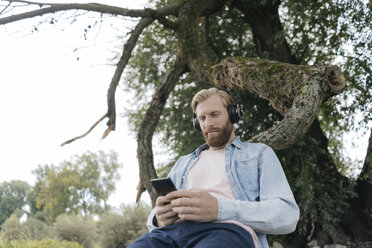 Man with smartphone and headphones listening music outdoors - KNSF03661