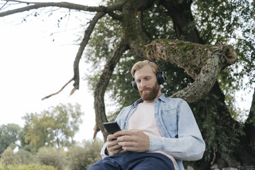 Mann mit Smartphone und Kopfhörern hört Musik im Freien - KNSF03661