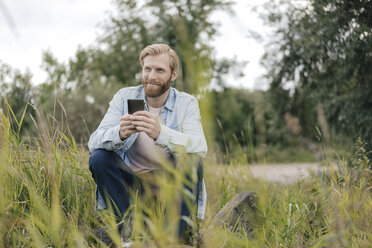 Lächelnder Mann benutzt Smartphone in der Natur - KNSF03668