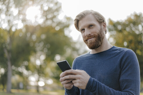 Porträt eines Mannes, der in einem Park ein Mobiltelefon benutzt - KNSF03679