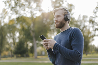 Mann hört Musik mit Kopfhörern und Smartphone in einem Park - KNSF03682