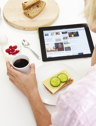 Frau benutzt digitales Tablet beim Frühstück, lizenzfreies Stockfoto