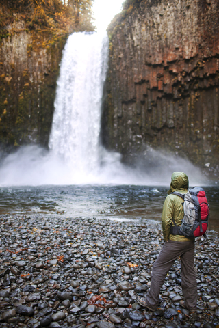 Wanderer steht auf Felsen vor einem Wasserfall, lizenzfreies Stockfoto