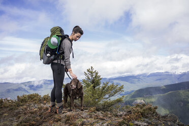 Woman standing with dog on mountain cliff against cloudy sky - CAVF33987