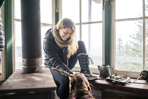 Glückliche Frau spielt mit Hund in Hütte, lizenzfreies Stockfoto