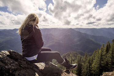 Woman sitting on rock at mountain cliff against cloudy sky - CAVF33996