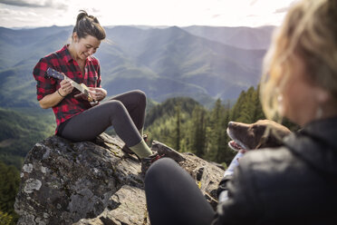 Frau spielt Ukulele auf einem Felsen an einer Bergklippe - CAVF34004