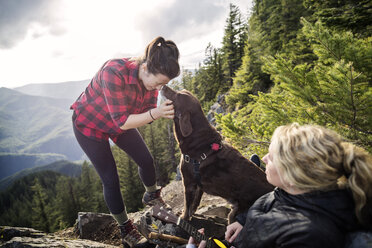 Women enjoying with dog on mountain cliff against sky - CAVF34009