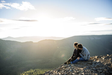 Paar sitzt auf einer Bergklippe und betrachtet die Aussicht - CAVF34022