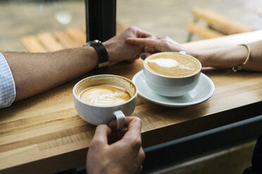 Abgeschnittenes Bild eines Paares, das sich bei einem Kaffee auf dem Tisch im Café die Hände hält - CAVF34026