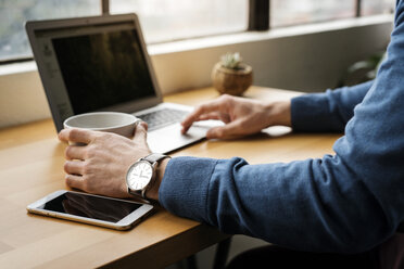 Cropped image of man using laptop on table in cafe - CAVF34031