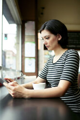 Young woman using tablet computer at cafe table - CAVF34042