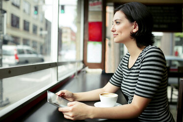 Nachdenkliche Frau, die einen Tablet-Computer hält und durch das Fenster eines Cafés schaut - CAVF34043