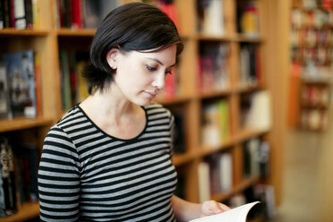 Young woman reading book in library - CAVF34044