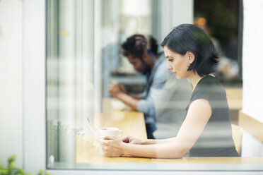 Side view of woman using tablet computer in cafe seen through glass window - CAVF34054