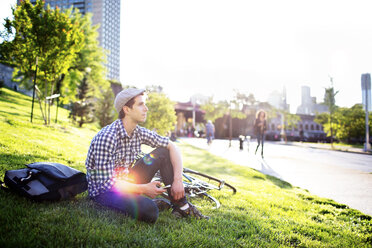 Thoughtful man sitting on grass field against clear sky - CAVF34069