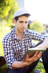 Mann, der ein digitales Tablet benutzt, während er auf einer Wiese sitzt - CAVF34070