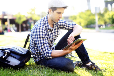 Man using digital tablet while sitting at grassy field on sunny day - CAVF34071