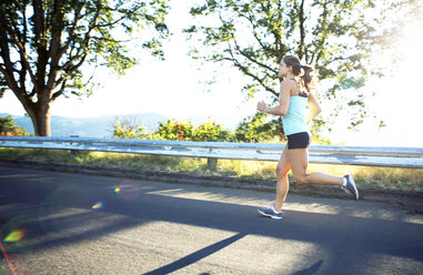 Side view of determined woman running on road during summer - CAVF34076