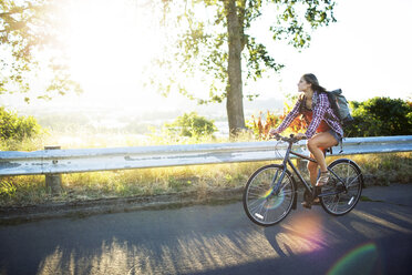 Junge Frau fährt mit dem Fahrrad auf der Straße im Sommer - CAVF34081