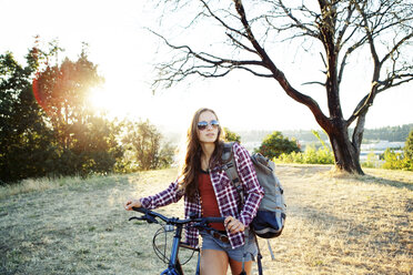 Junge Frau mit Fahrrad und Rucksack zu Fuß auf einem Feld - CAVF34085