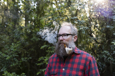 Man smoking pipe while standing against trees - CAVF34105