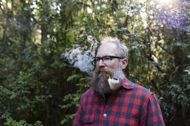 Mann raucht Pfeife, während er gegen Bäume steht - CAVF34105