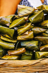 Close-up of food wrapped in banana leaves on basket - CAVF34125