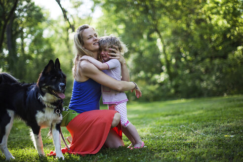 Mutter umarmt weinende Tochter von Hund auf Feld - CAVF34162