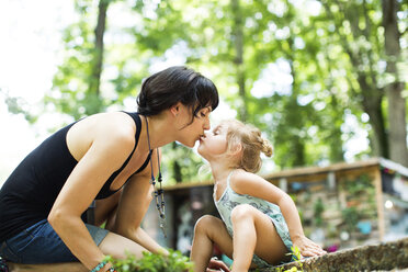 Loving daughter kissing mother on mouth while sitting in backyard - CAVF34171