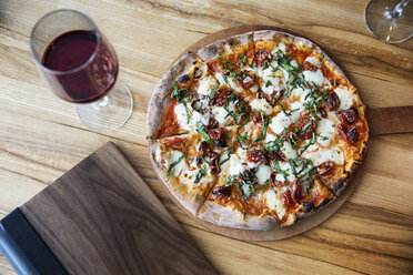 Draufsicht auf eine frische Pizza mit Rotweinglas auf einem Restauranttisch - CAVF34180