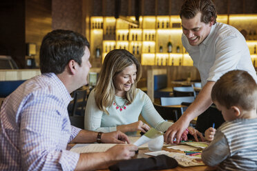 Glücklicher Kellner, der einer Familie beim Lesen der Speisekarte am Restauranttisch hilft - CAVF34187