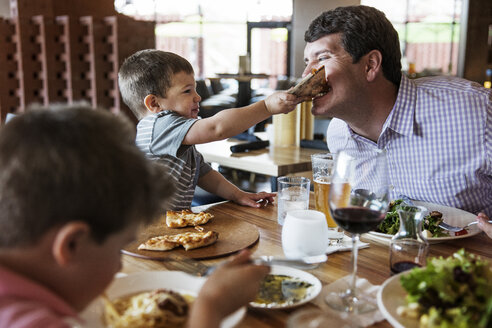 Boy feeding pizza to father in restaurant - CAVF34191