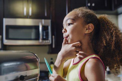 Nettes Mädchen leckt Daumen beim Backen in der Küche, lizenzfreies Stockfoto