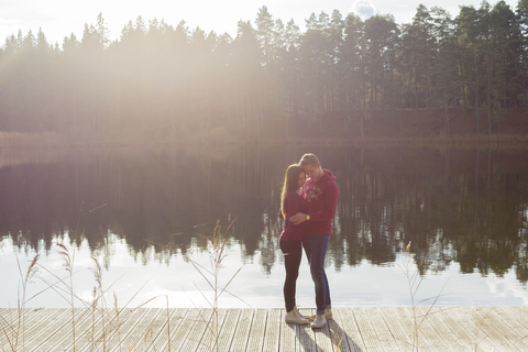 Umarmung eines Paares auf einem Steg am See, lizenzfreies Stockfoto