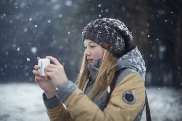Woman photographing through mobile phone during snowfall - CAVF34251