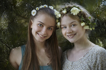 Porträt von glücklichen Freundinnen, die Tiaras tragen, während sie bei Pflanzen im Park stehen - CAVF34266
