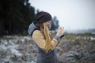 Frau fotografiert im Winter mit dem Handy - CAVF34272