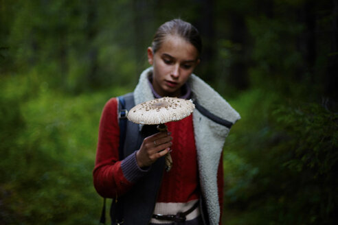 Teenager-Mädchen, das im Wald stehend einen großen Pilz betrachtet - CAVF34300