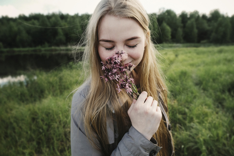 Frau riecht an Blumen und steht am See, lizenzfreies Stockfoto