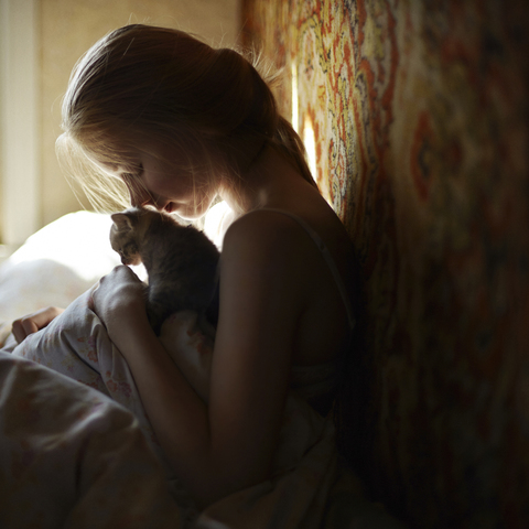 Seitenansicht einer Frau mit Katze auf dem Bett sitzend, lizenzfreies Stockfoto